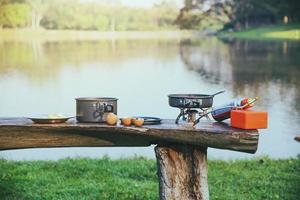 sullo sfondo la pentola e il picnic a gas che viene posizionato sul tavolo di legno. campeggio, picnic, cucina, mangiare in riva al lago. foto