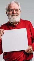 un' sorridente anziano uomo nel un' rosso maglione detiene un' vuoto bianca cartello foto