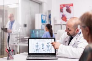 dottore che indica lo scheletro umano sul laptop foto