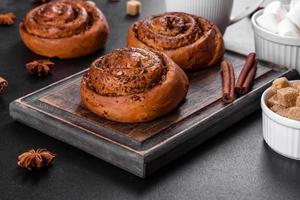 rotolo alla cannella appena sfornato con spezie e ripieno di cacao su fondo nero foto