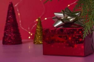 un regalo favoloso in una scatola rossa con un nastro d'oro sotto l'albero di natale, su uno sfondo rosa. capodanno e natale. copia spazio