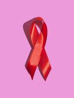 giornata internazionale dell'aiuto. nastro rosso con un'ombra dura su uno sfondo rosa. aiuta il concetto di consapevolezza. verticale foto