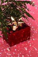 un regalo favoloso in una scatola rossa con un nastro d'oro sotto l'albero di natale, su uno sfondo rosa con bokeh. capodanno e natale.
