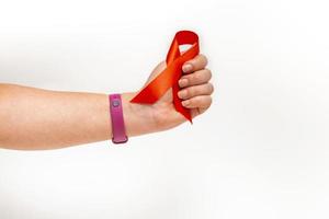 concetto medico per la giornata mondiale dell'AIDS a dicembre. il rosso aiuta il nastro di consapevolezza stretto nella mano di una donna su uno sfondo bianco. avvicinamento foto