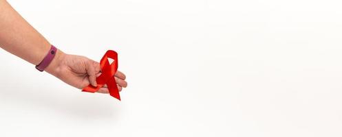 concetto medico per la giornata mondiale dell'AIDS a dicembre. il rosso aiuta il nastro di consapevolezza stretto nella mano di una donna su uno sfondo bianco. avvicinamento foto