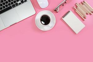 tavolo da lavoro piatto con computer portatile, forniture per ufficio, tazza da caffè, telefono cellulare, tablet e tazza da caffè su sfondo rosa foto