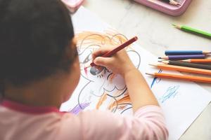 bambina che dipinge su un foglio di carta con matite colorate sul tavolo di legno a casa - impara il bambino a disegnare immagini e pastelli colorati