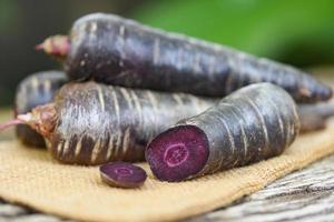 carota viola sul sacco, carota fresca per cucinare vegetariano su tavola di legno. foto