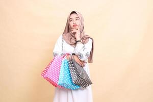il storia di un' giovane asiatico musulmano donna indossare un' hijab accigliato pensiero e trasporto shopping borse. per pubblicità, cultura, eid e Ramadan foto