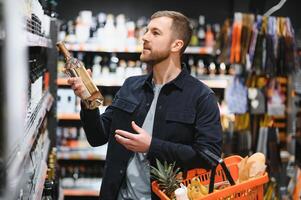 giovane uomo guardare a bottiglia di vino nel supermercato foto