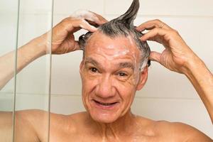 uomo maturo che fa la doccia e si lava i capelli con lo shampoo foto