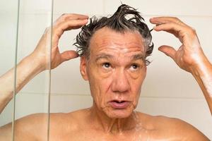 uomo maturo che fa la doccia e si lava i capelli con lo shampoo foto