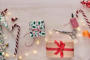 composizione di natale. scatole regalo, regali incartati con carta e nastro, luci, bastoncini di zucchero su fondo di legno. Holdiay fai da te decorazioni per la casa fatte a mano. inverno, capodanno disteso, vista dall'alto foto