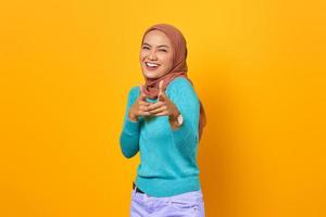 sorridente giovane donna asiatica che punta il dito in telecamera su sfondo giallo foto