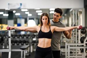 personal trainer che aiuta una giovane donna a sollevare pesi foto