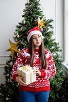 giovane donna in maglione rosso che tiene un regalo di natale foto