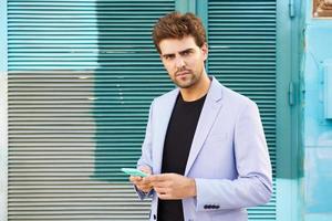 giovane imprenditore che indossa tuta blu utilizzando uno smartphone in background urbano. foto