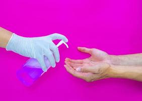 una mano guantata che spruzza un disinfettante per le mani dall'altro per proteggerla dai batteri e mantenerla igienica. foto