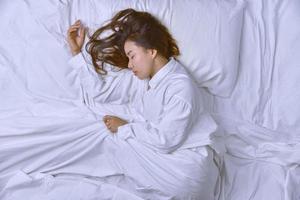 giovane donna che dorme nel letto. vista dall'alto della giovane donna sdraiata che dorme bene a letto. dormire rilassati, la giovane bella signora sorridente giace a letto. foto