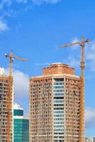 le gru a torre sono ancorate a moderni edifici residenziali in costruzione su uno sfondo di cielo blu. foto