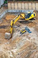 un grande escavatore giallo scava una fossa di fondazione in un cantiere edile. foto