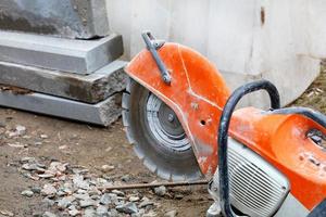 una taglierina a benzina con un disco diamantato davanti a un cantiere edile e parapetti in cemento. foto