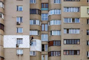 un costruttore di scalatori su una piattaforma sospesa isola la facciata di un appartamento separato in un edificio a più piani con plastica espansa bianca. foto