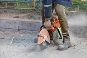 un lavoratore utilizza una motosega portatile e un disco da taglio diamantato per tagliare il vecchio asfalto sulla strada. foto