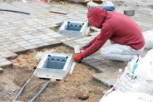 un operaio installa pozzi di servizio e posa le lastre di pavimentazione intorno ad essi. foto