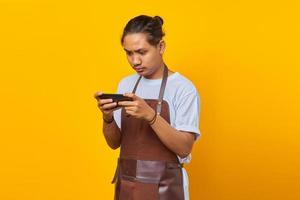 attraente giovane barista asiatico che utilizza il telefono cellulare per giocare su sfondo giallo