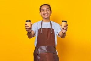 ritratto di un allegro barista che tiene in mano due tazze di caffè di carta tra cui scegliere isolato su sfondo giallo foto