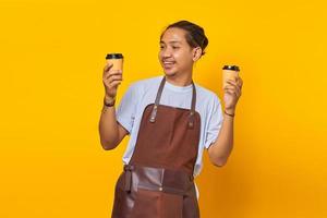 ritratto di un allegro barista che tiene in mano due tazze di caffè di carta tra cui scegliere isolato su sfondo giallo foto