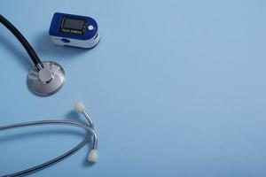 composizione piatta con pulsossimetro e stetoscopio su sfondo blu.un pulsossimetro utilizzato per misurare la frequenza cardiaca e i livelli di ossigeno.
