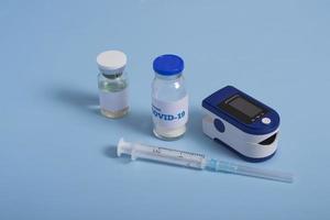 vaccino o modello di medicina. pulsossimetro, vaccino contro il coronavirus e siringa su sfondo blu. diagnosi di covid 19. banner pandemia 2021 foto