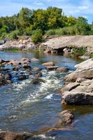 un rapido flusso d'acqua da un fiume di montagna scorre attraverso rapide di pietra in una giornata estiva. immagine verticale. foto