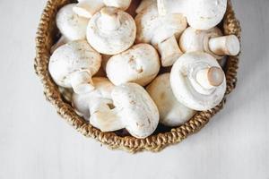 funghi champignon in un cesto di vimini rotondo su un tavolo di legno bianco foto