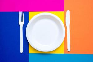 forchetta, coltello e piatto in plastica bianca su sfondo multicolore foto