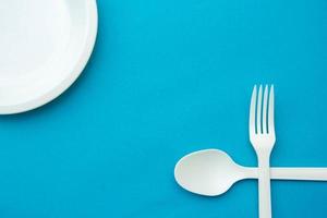 forchetta, cucchiaio e piatto incrociati in plastica bianca su sfondo blu