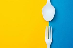 cucchiaio e forchetta di plastica bianca su sfondo giallo e blu foto