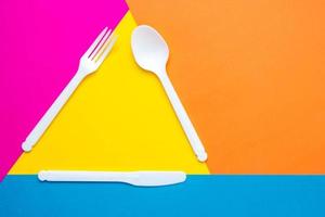 forchetta, coltello e cucchiaio in plastica bianca su sfondo multicolore