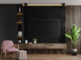 mockup di una parete tv montata in una stanza buia con poltrona e pianta su sfondo muro di marmo scuro. foto