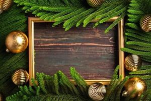 cornice dorata di natale con foglia di pino e decorazioni di palline su tavola di legno foto