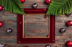 cornice rossa natalizia con foglia di pino e decorazioni con palline su tavola di legno foto