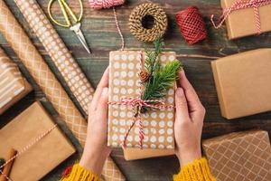 corda legata a mano su scatola regalo di natale con decorazioni in carta marrone con abete di pino su tavola di legno
