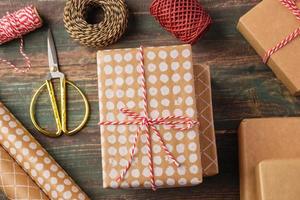 confezione regalo natalizia fatta a mano con decorazioni in carta marrone con abete di pino su tavola di legno foto