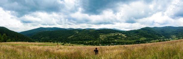 il ragazzo è seduto su una montagna verde e gode di un panorama incantevole foto