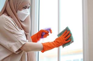 donna musulmana che pulisce il vetro della porta con tessuto e spray alcolico. foto