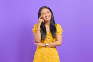 ritratto di giovane donna asiatica sorridente che pensa a un'idea e distoglie lo sguardo su sfondo viola foto