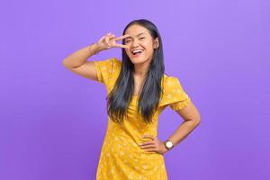 la giovane donna asiatica sorridente che mostra pace o vittoria firma sopra l'occhio su fondo porpora foto