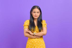 sorridente giovane donna asiatica con le braccia incrociate guardando la telecamera su sfondo viola foto